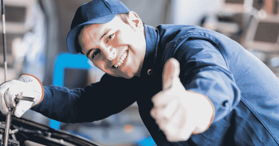 Mecânico sorridente faz sinal de positivo, representando uma boa gestão de pessoas na oficina.