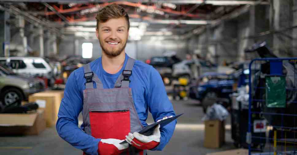 Mecânico sorridente segura prancheta com dados de indicadores simples na oficina.