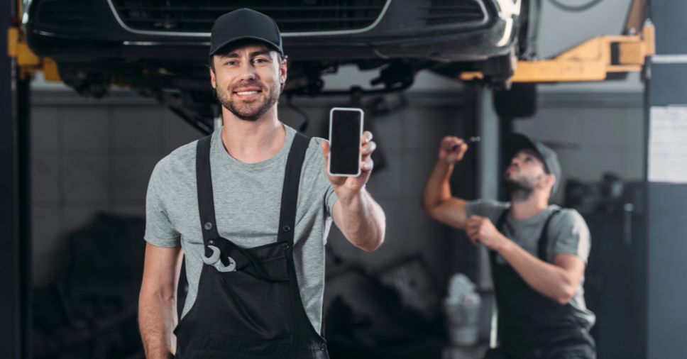 Mecânico sorri segurando celular para uso de inteligência artificial no diagnóstico e gestão.