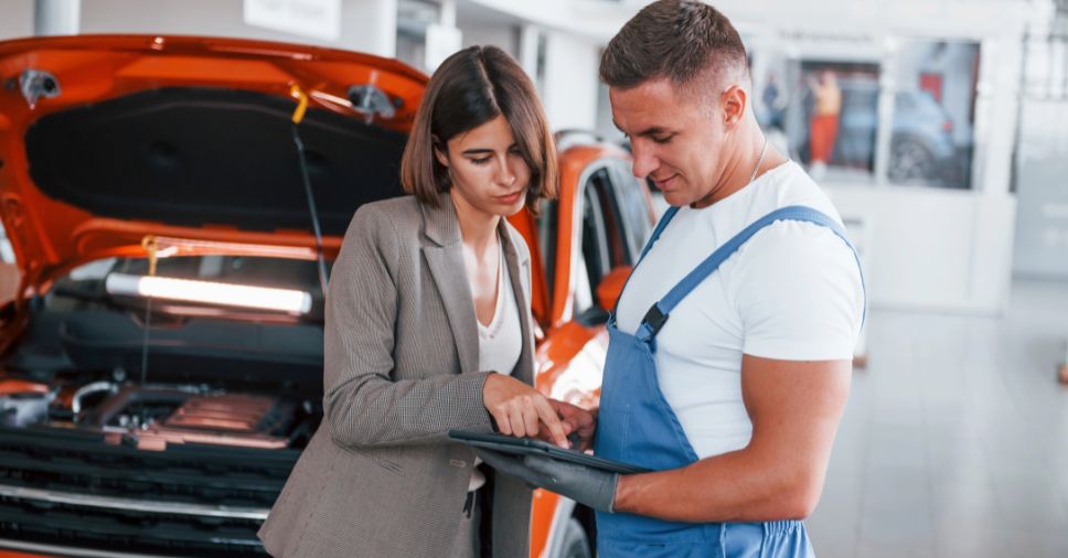 Funcionária e mecânico analisam tablet em oficina para aplicar o efeito Disney no atendimento.