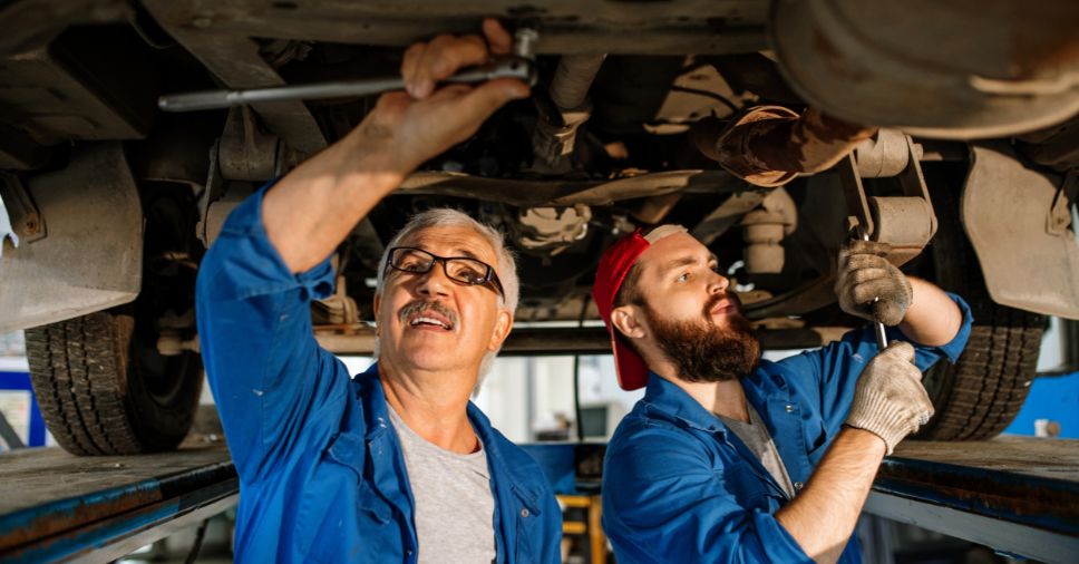 Detalhe de homens consertando motor e escapamento mostra a produtividade dos mecânicos.