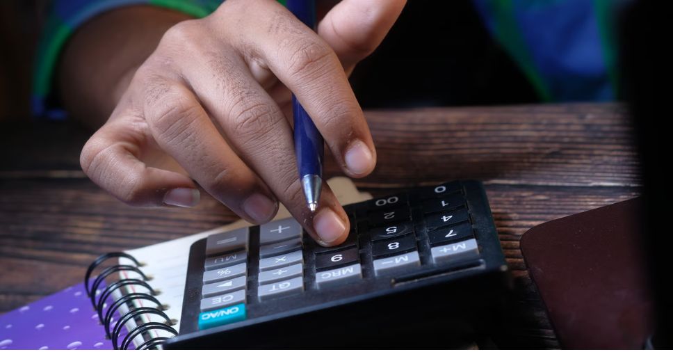 Pessoa efetuando contas com calculadora, representando o levantamento e impacto do custo invisível.
